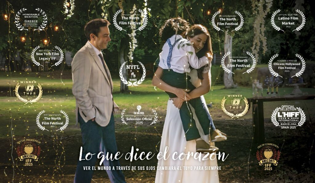 Scene from the film Lo que dice el corazón: a man in a light jacket and jeans looks at a woman in a white dress hugging a child, surrounded by festival award laurels.
